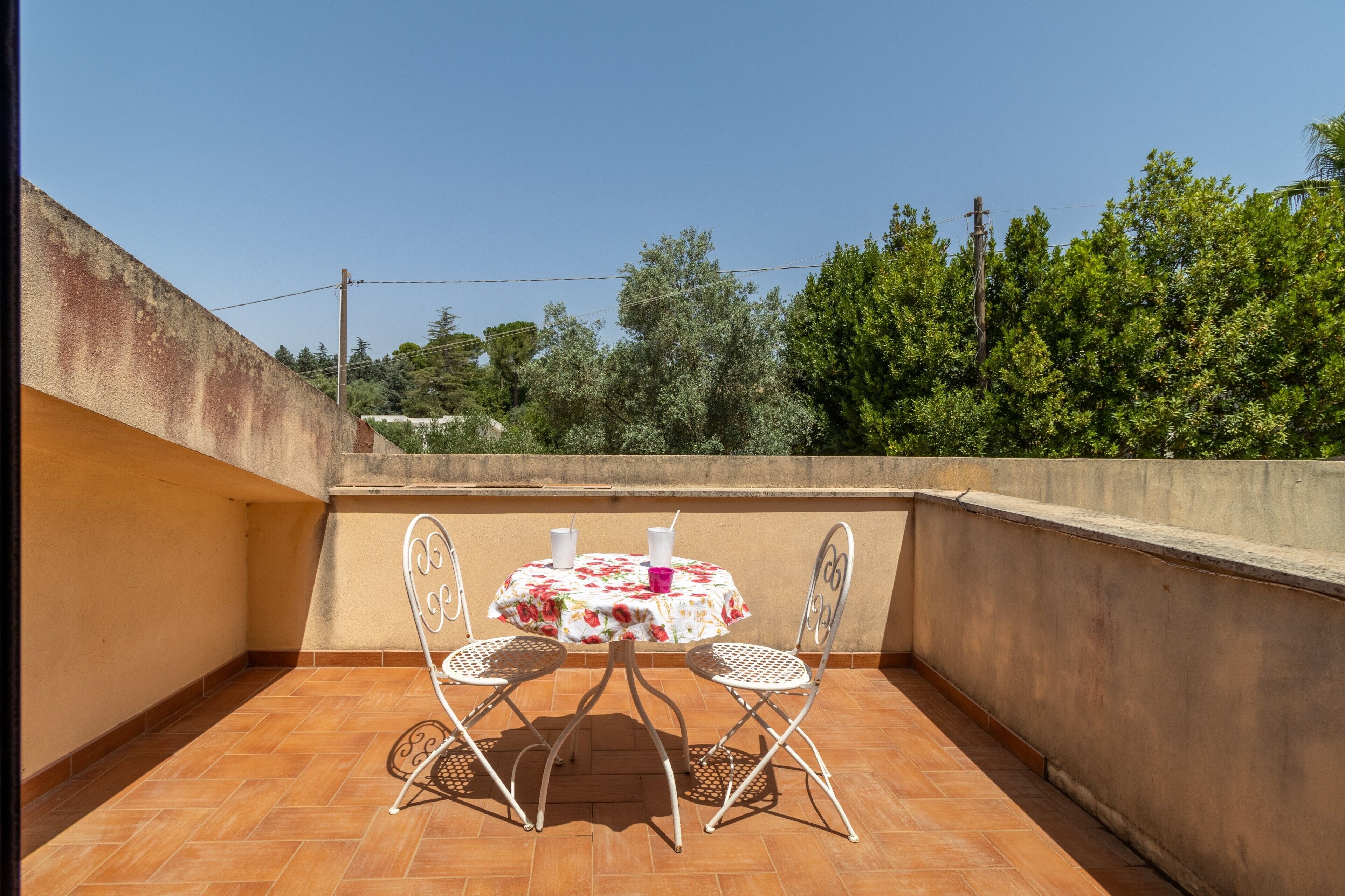 Une terrasse avec une table et des chaises, un sol carrelé et une vue sur les arbres et les lignes électriques.