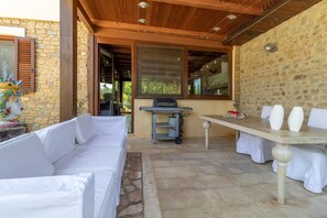 Une terrasse extérieure avec un canapé blanc, une table ornée de vases et un chariot muni d’un distributeur d’eau.