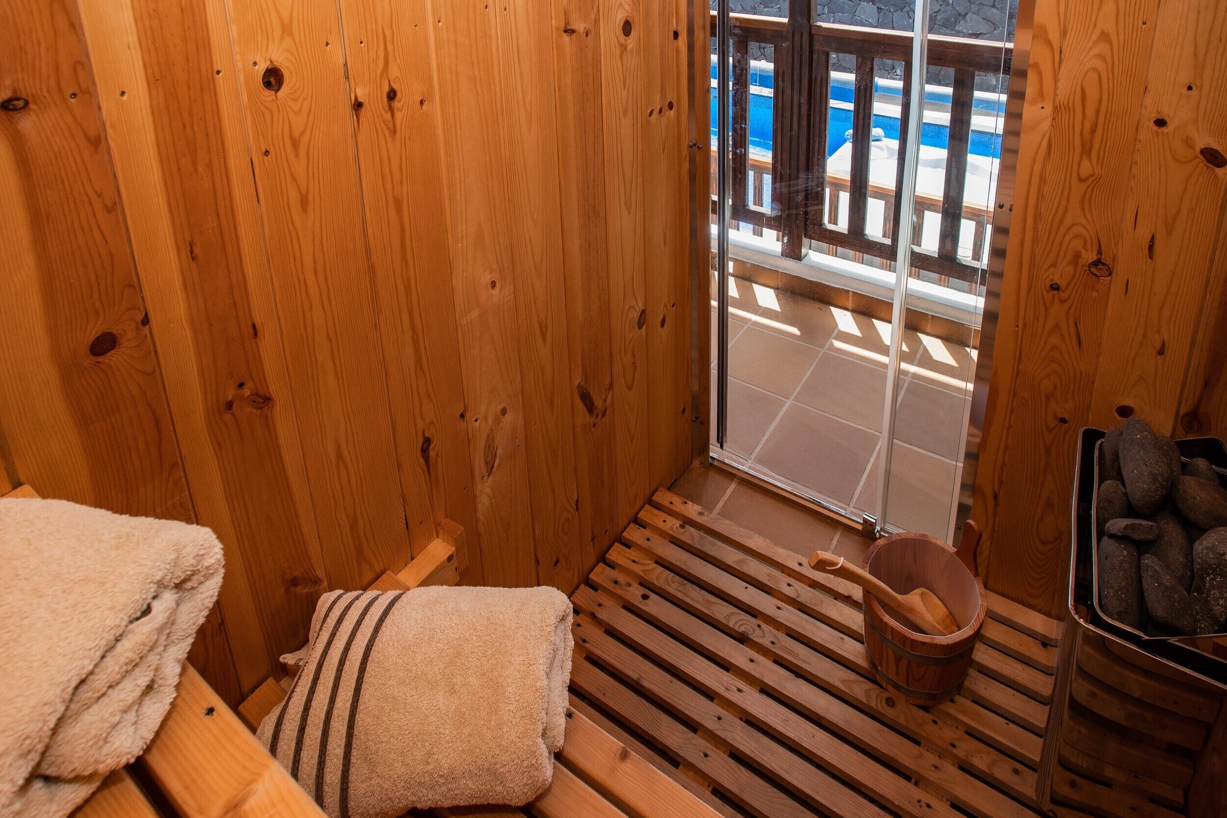 Een houten sauna met een bank, een handdoek, een emmer en een stenen bak.
