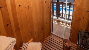 Una sauna de madera con un banco, una toalla, un cubo y un recipiente de piedra.