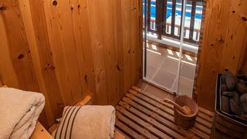 Een houten sauna met een bank, een handdoek, een emmer en een stenen bak.