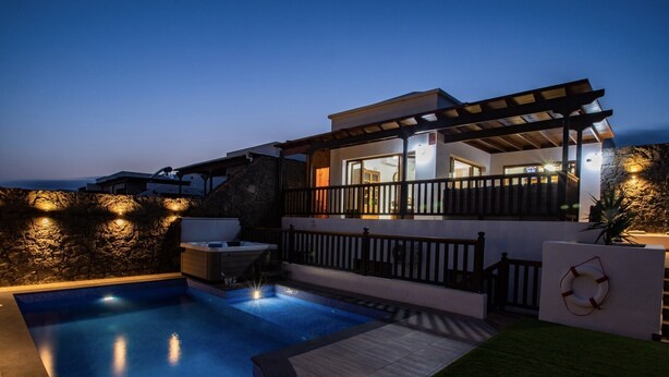 Una casa moderna con piscina, un porche cubierto y un muro de piedra.