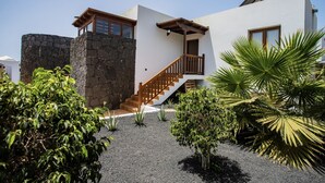 Una casa moderna con un muro de piedra, una escalera de madera y un pequeño jardín con palmeras.