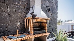 Un muro de piedra con un horno de ladrillo, un banco de madera y una planta en maceta.