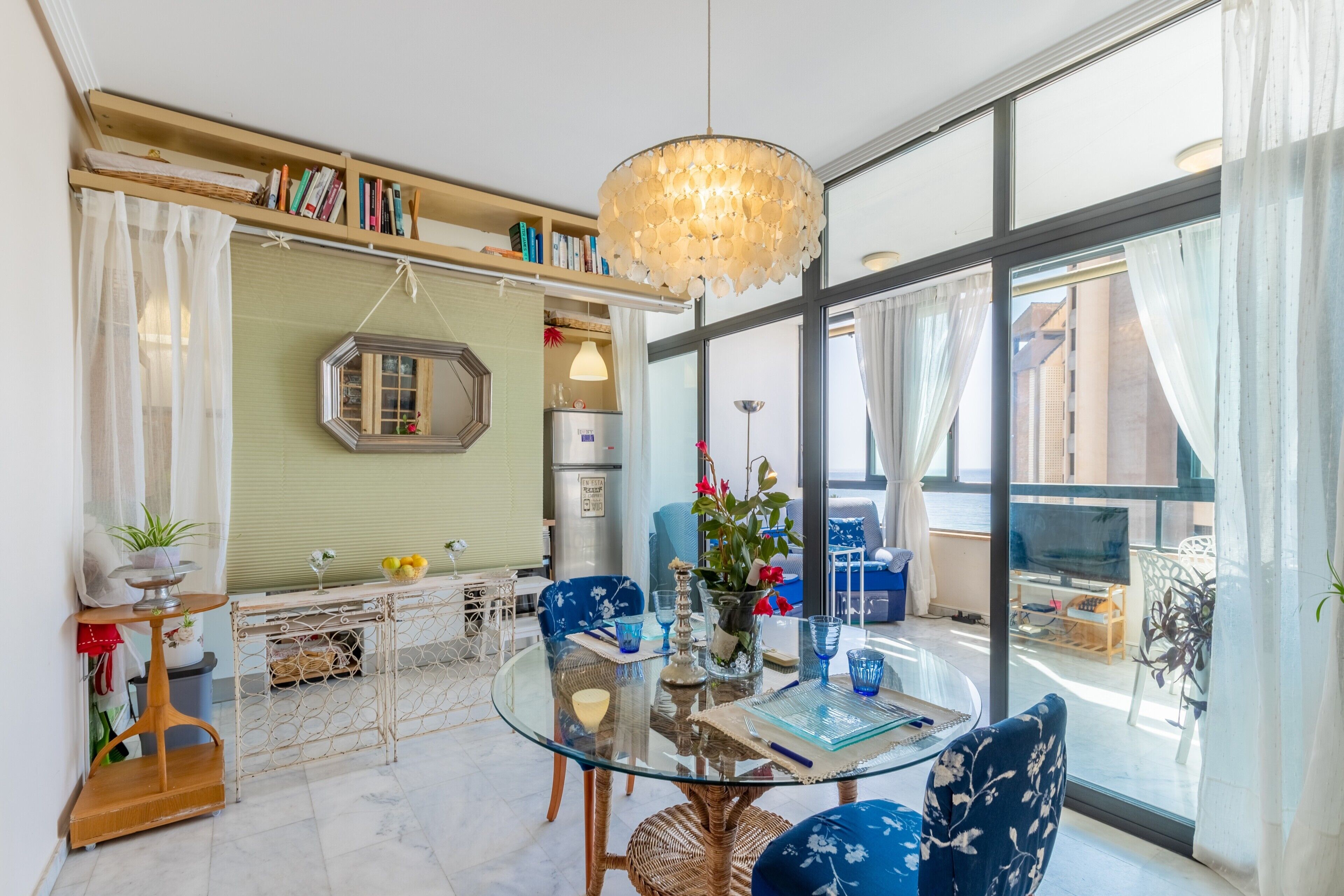 A modern living room with a glass table, blue chairs, a hanging light fixture, and a view of the outside. - Apartment 'Apartamento Paraíso Florida' with Sea View, Wi-Fi and Air Conditioning (Benidorm)