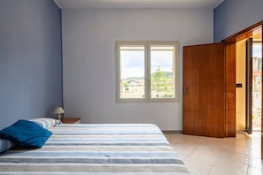 Une chambre à coucher avec un lit, une fenêtre, une table de chevet et une porte en bois.