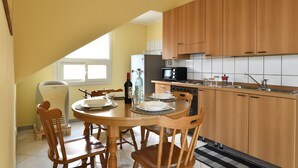 A kitchen with wooden cabinets, a dining table with chairs, a refrigerator, and a microwave. - Holiday Apartment "Corbezzolo" with Balcony & Shared Terrace (Bari sardo)