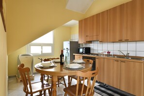 Une cuisine avec des meubles de rangement en bois, une table à manger avec des chaises, un réfrigérateur et un four à micro-ondes.