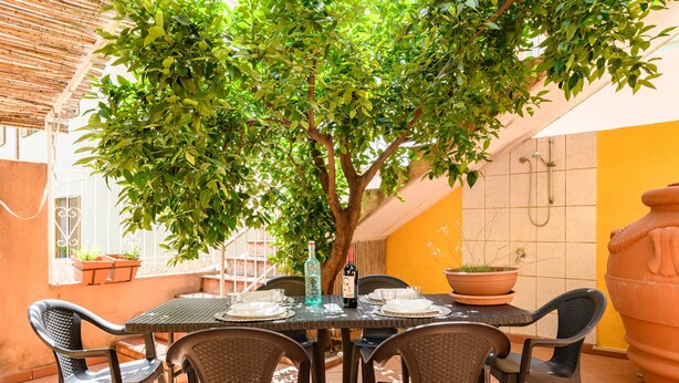 An outdoor dining area with a table set for four, surrounded by wicker chairs, under a tree. - Holiday Apartment "Corbezzolo" with Balcony & Shared Terrace (Bari sardo)