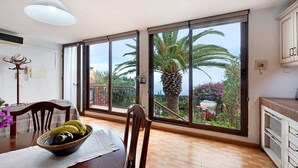 Un comedor con una mesa, sillas, un cuenco de fruta y vistas a una palmera a través de amplios ventanales.