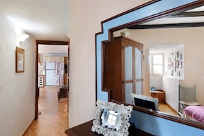 A hallway with a wooden floor, a mirror reflecting a room with a bed and a chair, and a doorway leading to a kitchen area. - Holiday Home "Casa Titi" with Sea View, Private Terrace and Wi-Fi (La Palma)