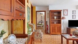 Una sala de estar con muebles de madera, un televisor y un pasillo que da a un dormitorio.