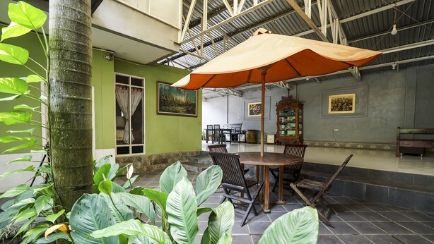 An indoor patio area with a dining table, chairs, a large umbrella, and lush green plants. - OYO Life 91027 Note Hotel Syariah (Prabumulih)
