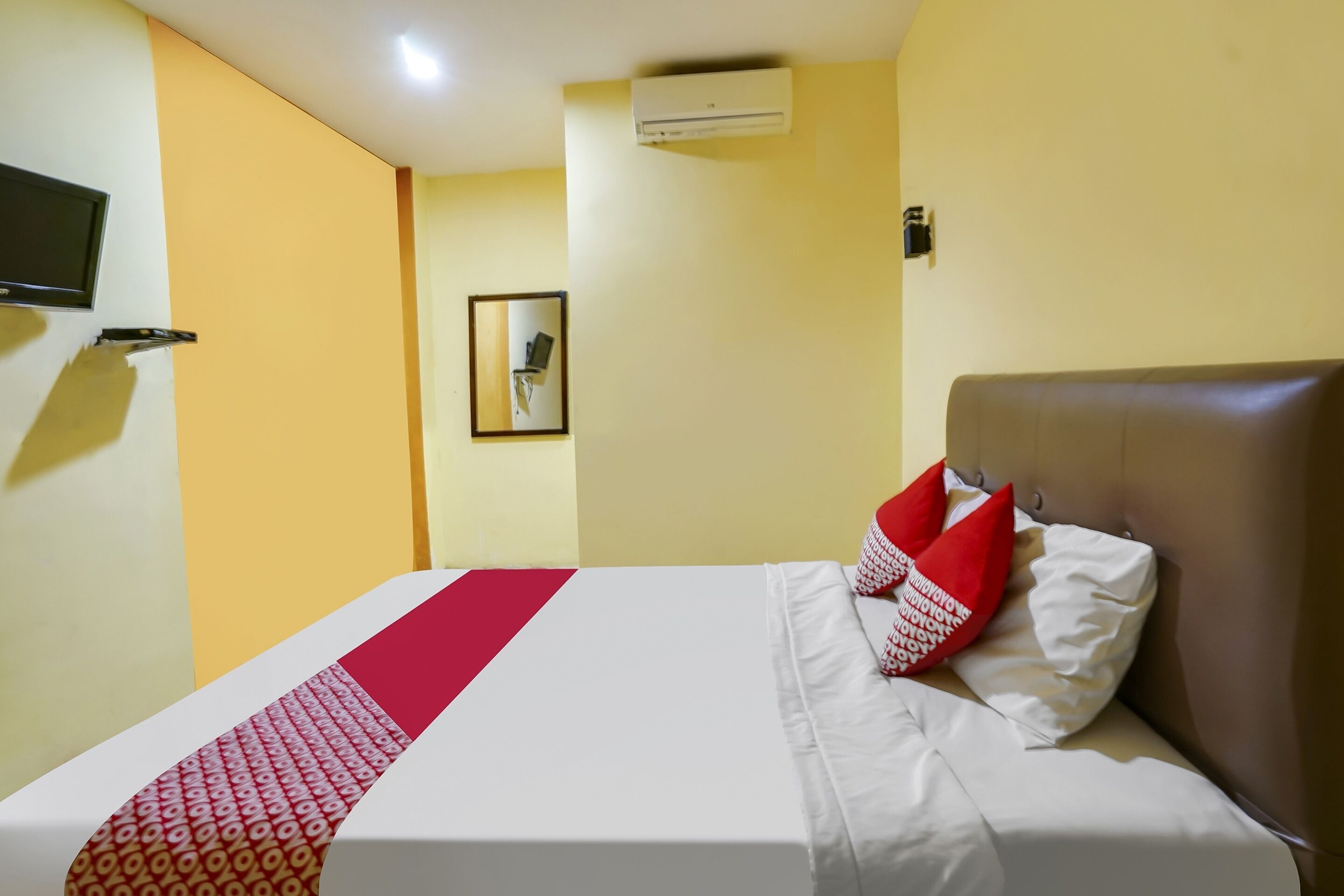 Ein Hotelzimmer mit einem Bett, einem Wand-Fernseher, einer Klimaanlage und einem gerahmten Bild an der Wand.