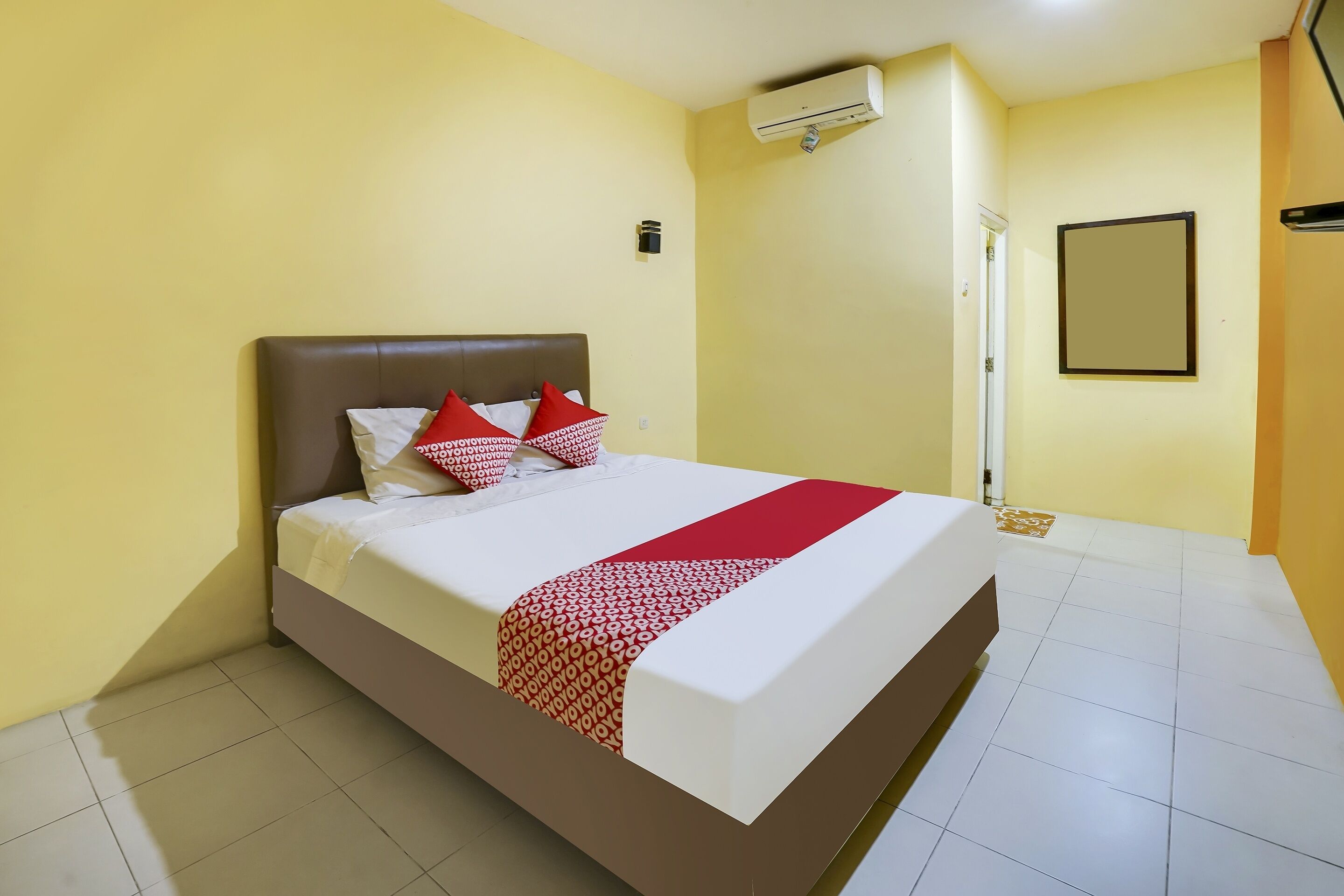 A hotel room with a bed, a red and white patterned bedspread, and a red throw blanket.