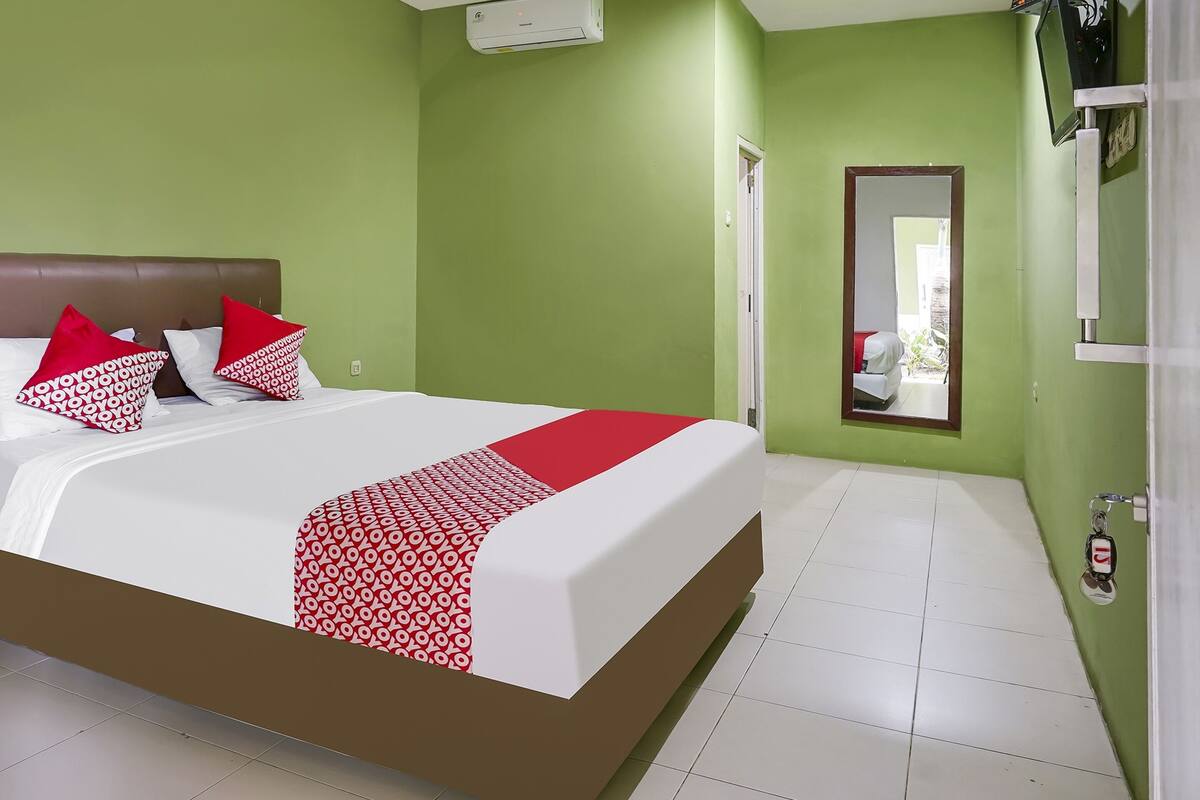 Quarto de hotel com uma cama grande, paredes verdes, piso de azulejos brancos e uma porta que dá para outro quarto.