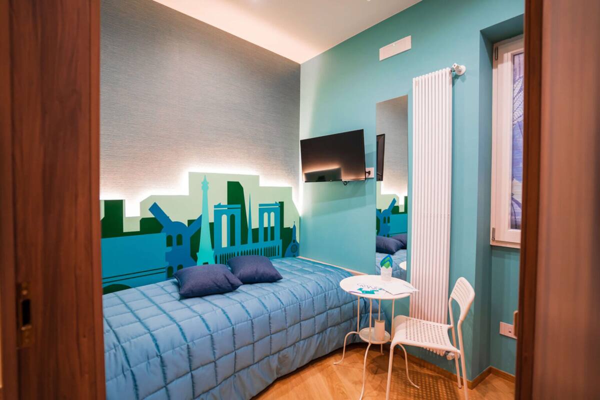 A bedroom with a bed, a chair, a table, a TV, and a radiator.