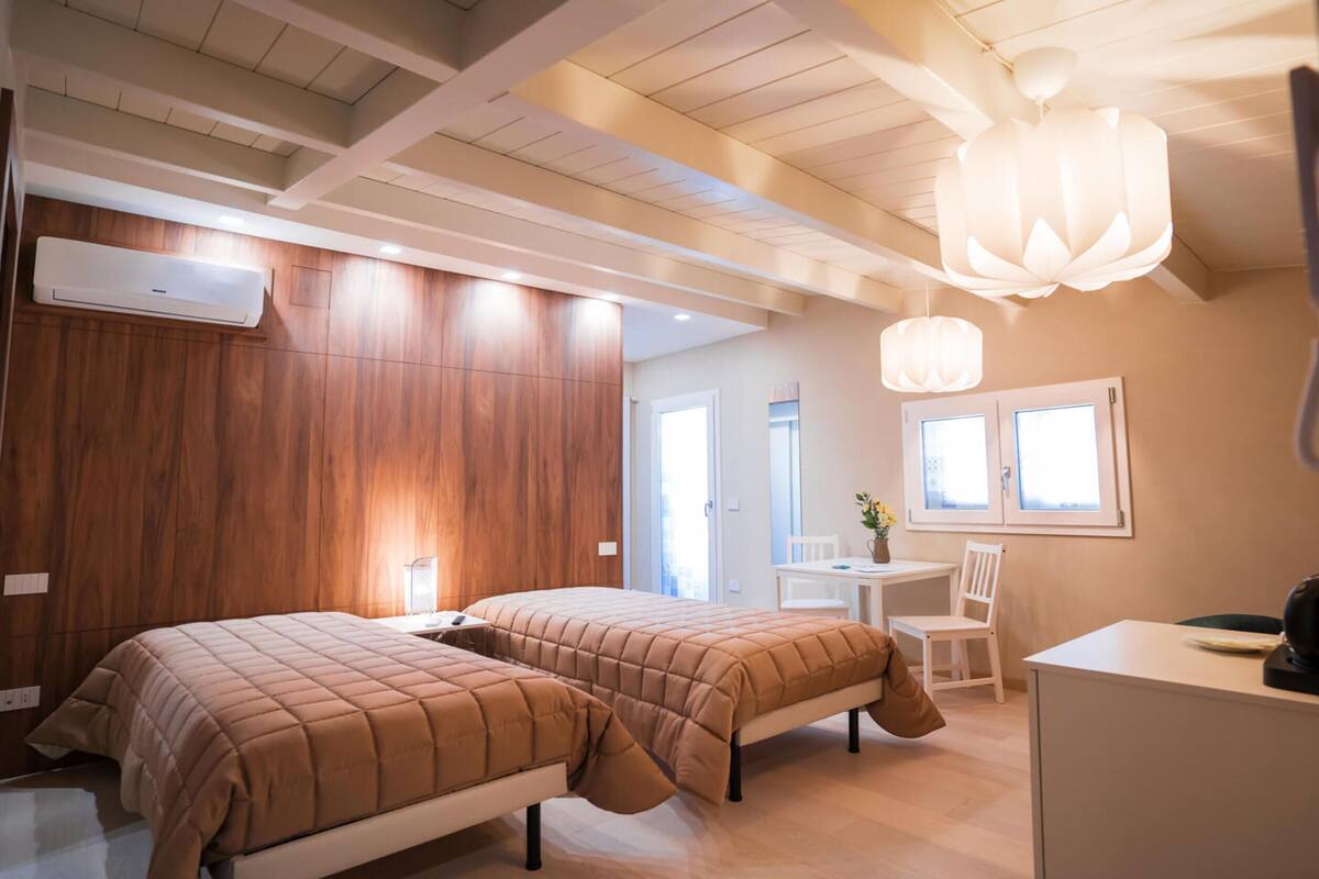 A hotel room with two beds, a desk, a chair, a window, and a ceiling fan.
