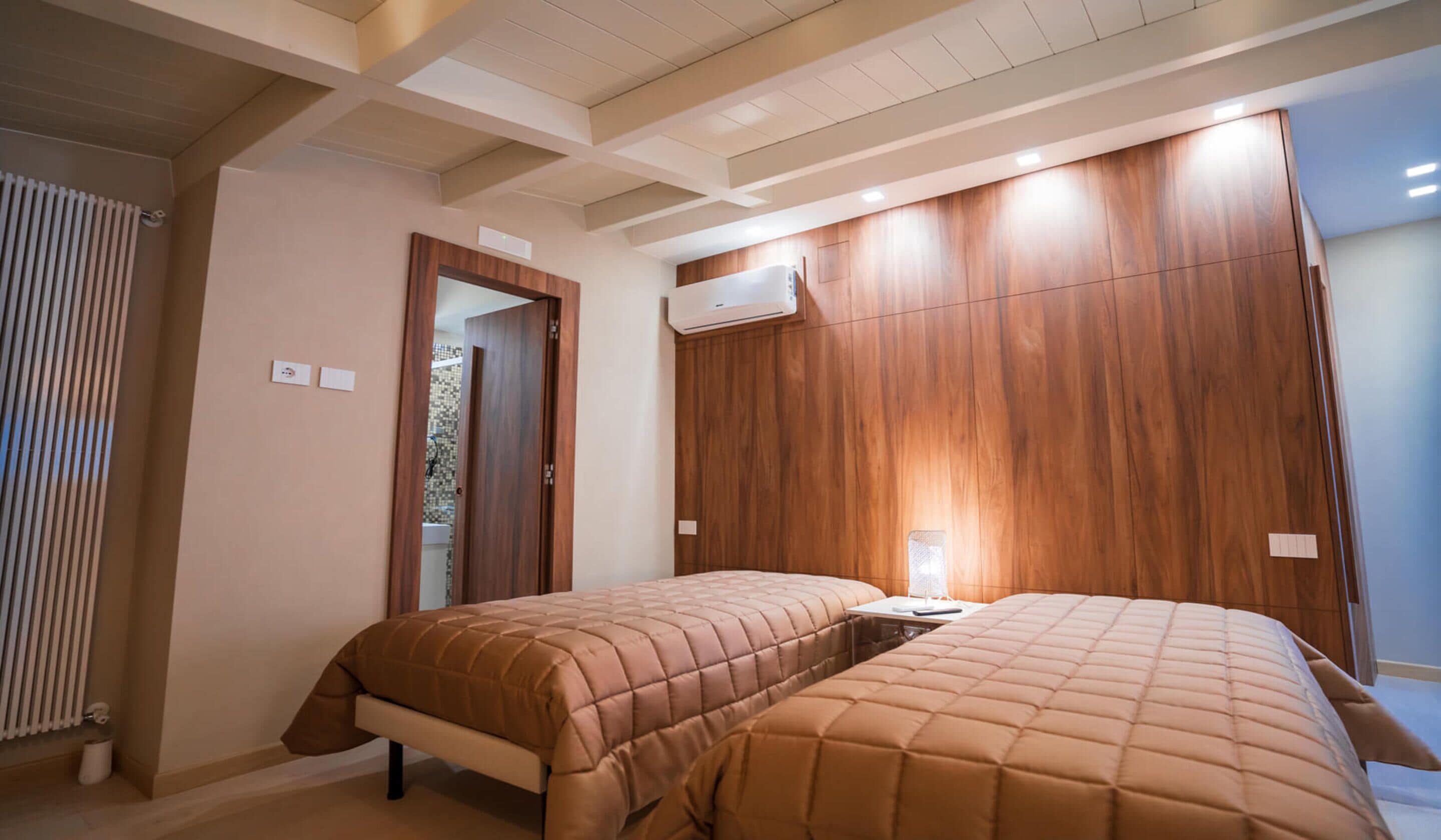 A bedroom with two beds, wooden paneling on the walls, an air conditioning unit, and a radiator.
