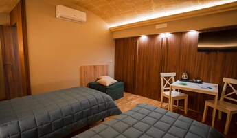 Una habitación con dos camas, un escritorio con sillas, un televisor y paneles de madera en las paredes.