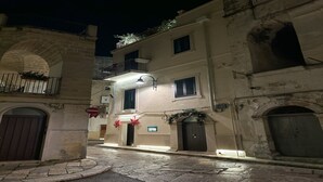 Uma rua estreita com calçada de pedra, edifícios históricos com varandas e uma placa indicando um espaço público.