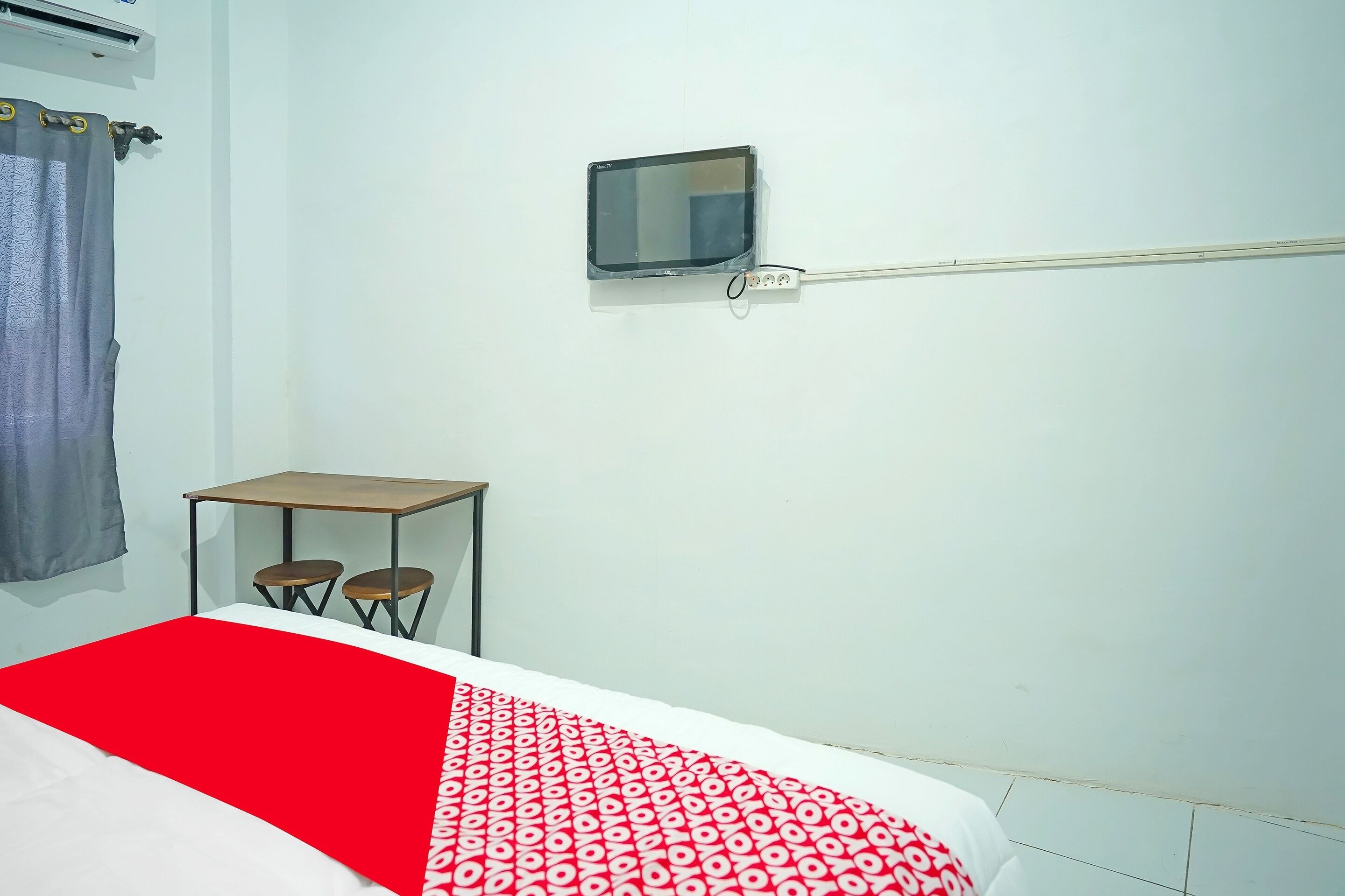 Quarto com cama, uma pequena mesa com duas cadeiras, televisão fixada na parede e ar condicionado.