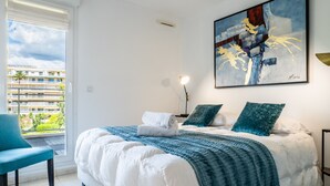 Ein Schlafzimmer mit einem großen Bett, Blick auf ein Gebäude durch ein Fenster und einem Gemälde an der Wand.