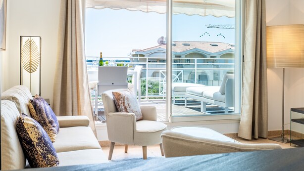 Ein Hotelzimmer mit einer großen Schiebeglasdoor, die auf einen Balkon mit Sitzmöbeln führt.