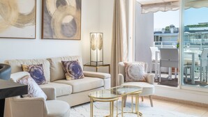 Ein modernes Wohnzimmer mit einer Couch, Sesseln, einem Glastisch und Kunstwerken an der Wand.