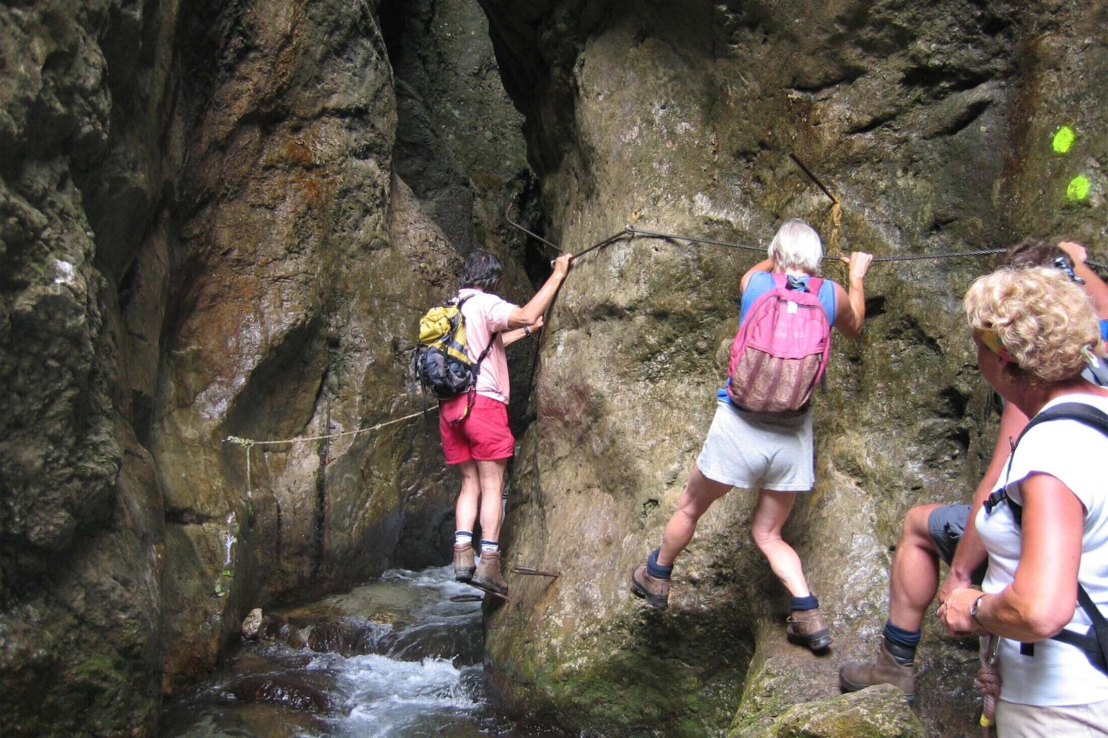 A group of hikers navigating a narrow rocky passage with a stream below.