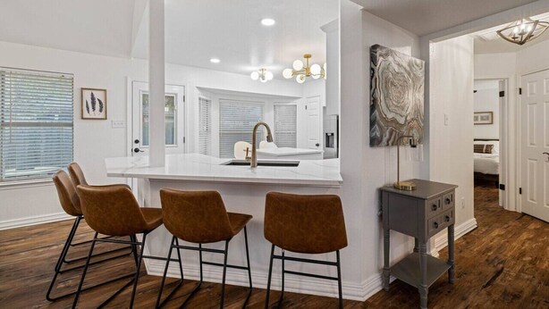 A modern kitchen with a central island, bar stools, a pendant light, and a decorative wall piece. - Modern Comfort: WiFi, 3BR, King, Patio (Round Rock)