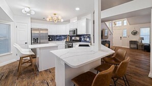 A modern kitchen with white cabinetry, a central island, and a dining area with brown chairs. - Modern Comfort: WiFi, 3BR, King, Patio (Round Rock)