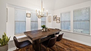 A dining room with a wooden table, four chairs, a chandelier, and large windows with blinds. - Modern Comfort: WiFi, 3BR, King, Patio (Round Rock)