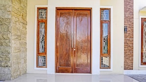 A building with a large wooden double door, two windows with metal bars, and a stone wall on one side. - Hotel O Reva Residence Syariah (Kamal)