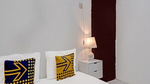 A bedroom with a bed, two pillows with geometric patterns, a bedside table with a lamp, and a dark wall. - Hotel O Reva Residence Syariah (Kamal)