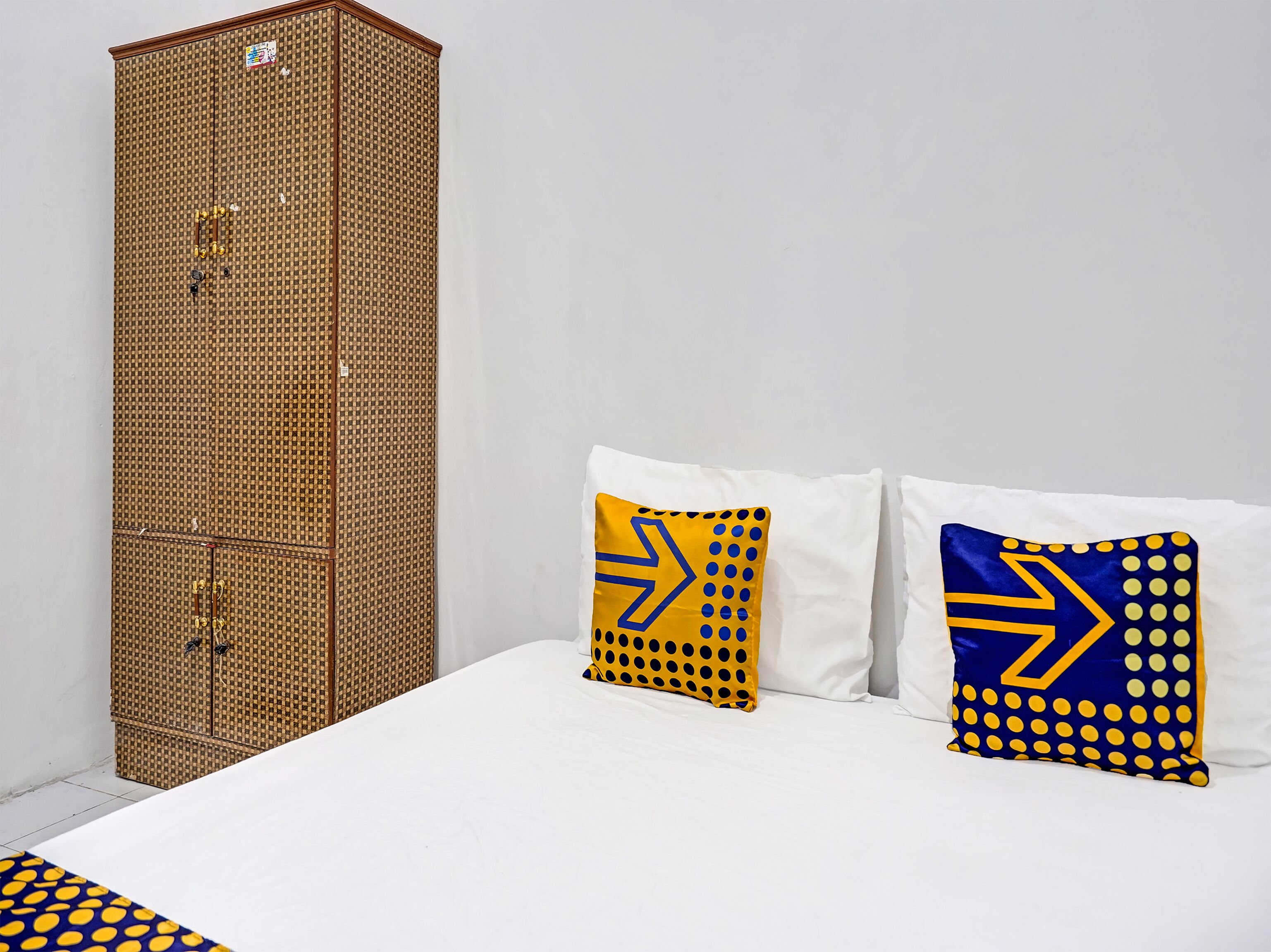 A room with a bed, two pillows with geometric patterns, and a tall, woven cabinet.