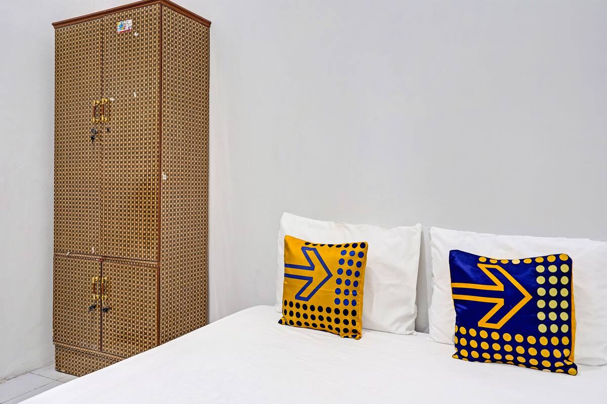 A room with a bed, two pillows with geometric patterns, and a tall, woven cabinet.