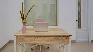 A wooden desk with a laptop, a pink vase with decorative elements, and a chair. - Hotel O Reva Residence Syariah (Kamal)