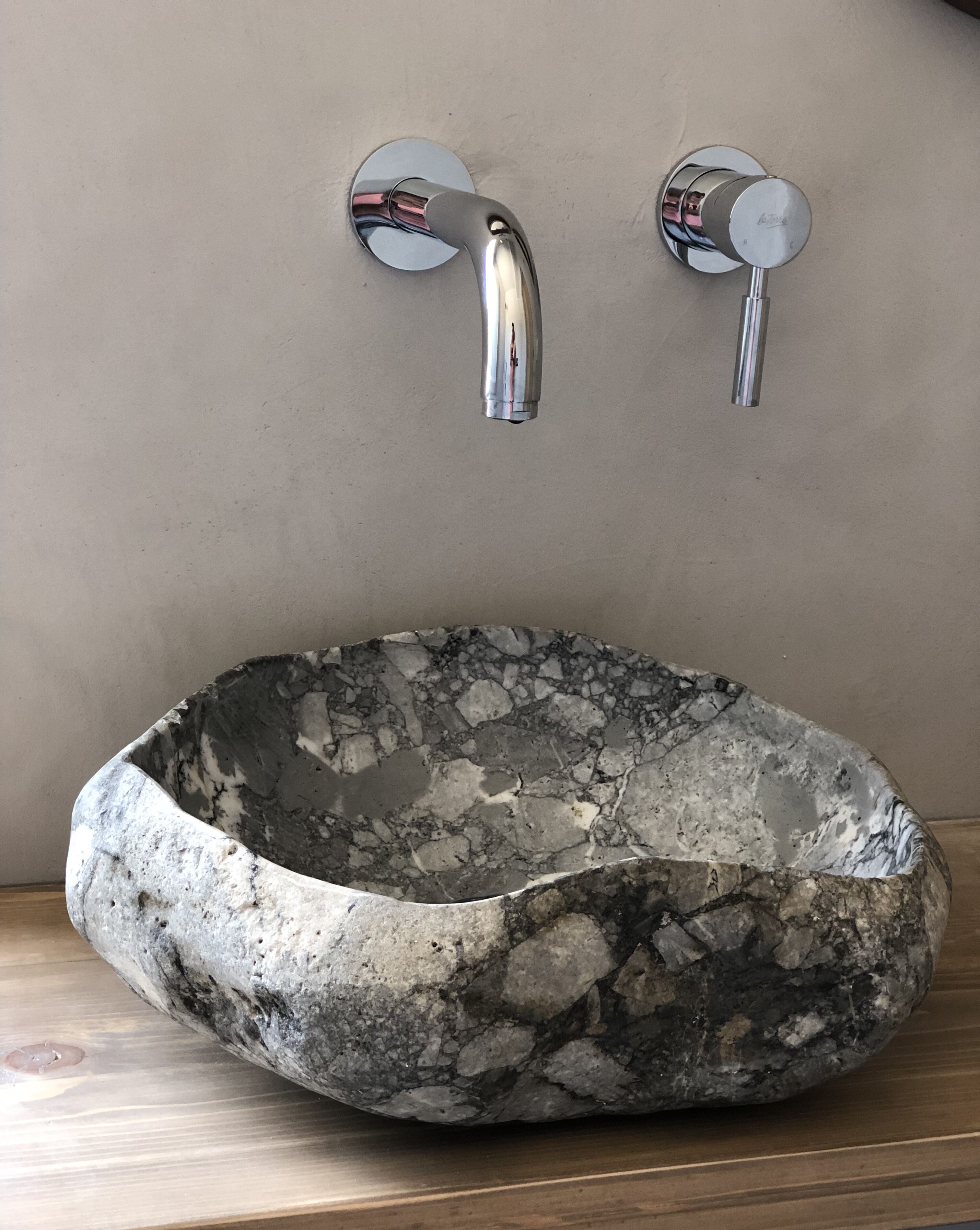 Ein steinernes Waschbecken mit einem modernen Wasserhahn an einer beige gefärbten Wand.