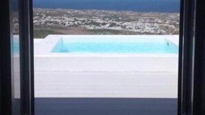 Vista des d'una finestra d'una zona de piscina sota un cel clar i un paisatge llunyà.