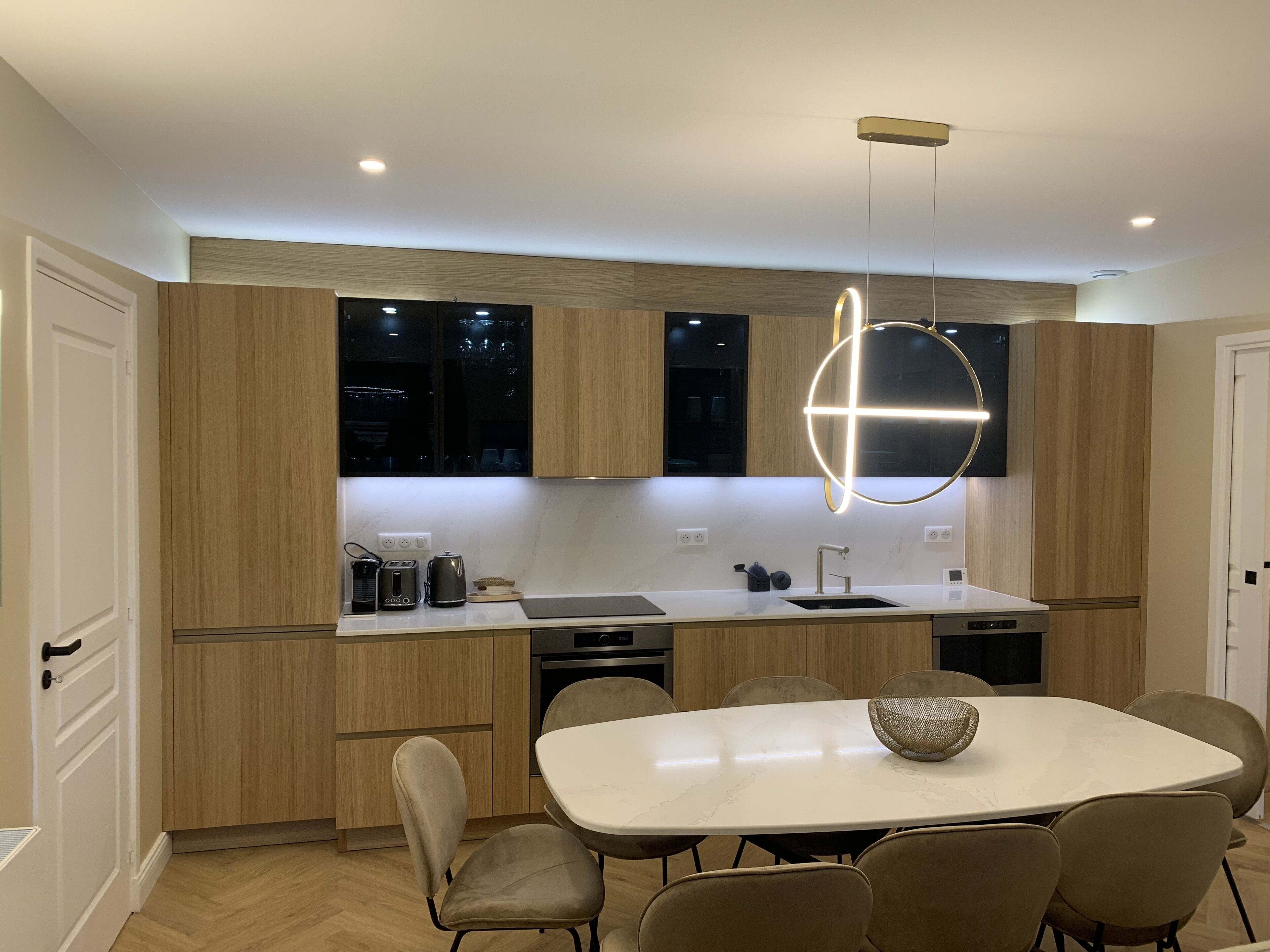 A modern kitchen with wooden cabinets, a white countertop, and a dining area with a marble table and chairs.
