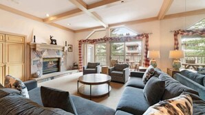 A spacious living room with a fireplace, comfortable seating, and large windows offering a view of the outdoors. - Saint James Place PL4 (Avon)