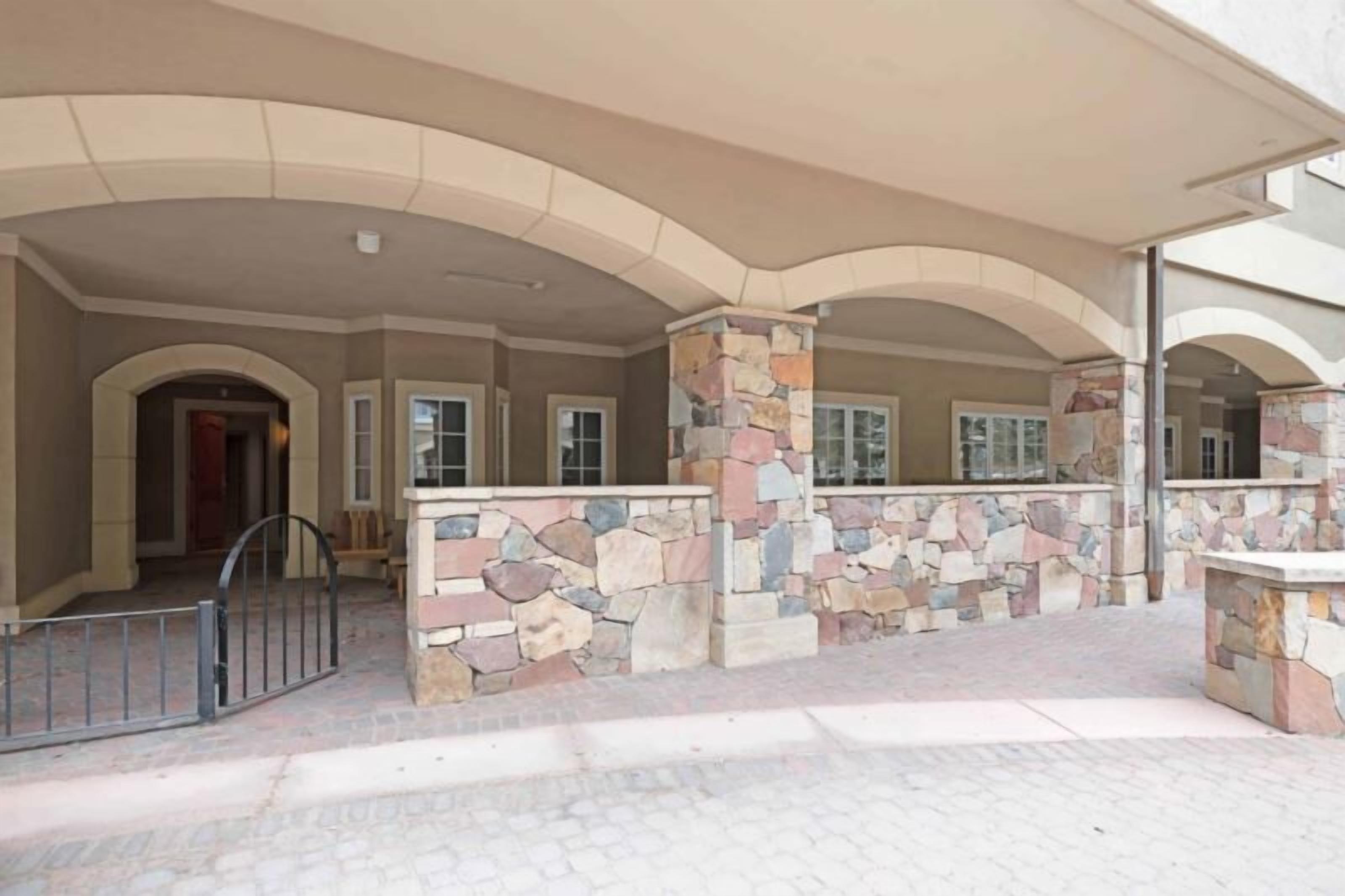 A covered outdoor area with stone pillars and arches, a gated entrance, and a paved walkway.