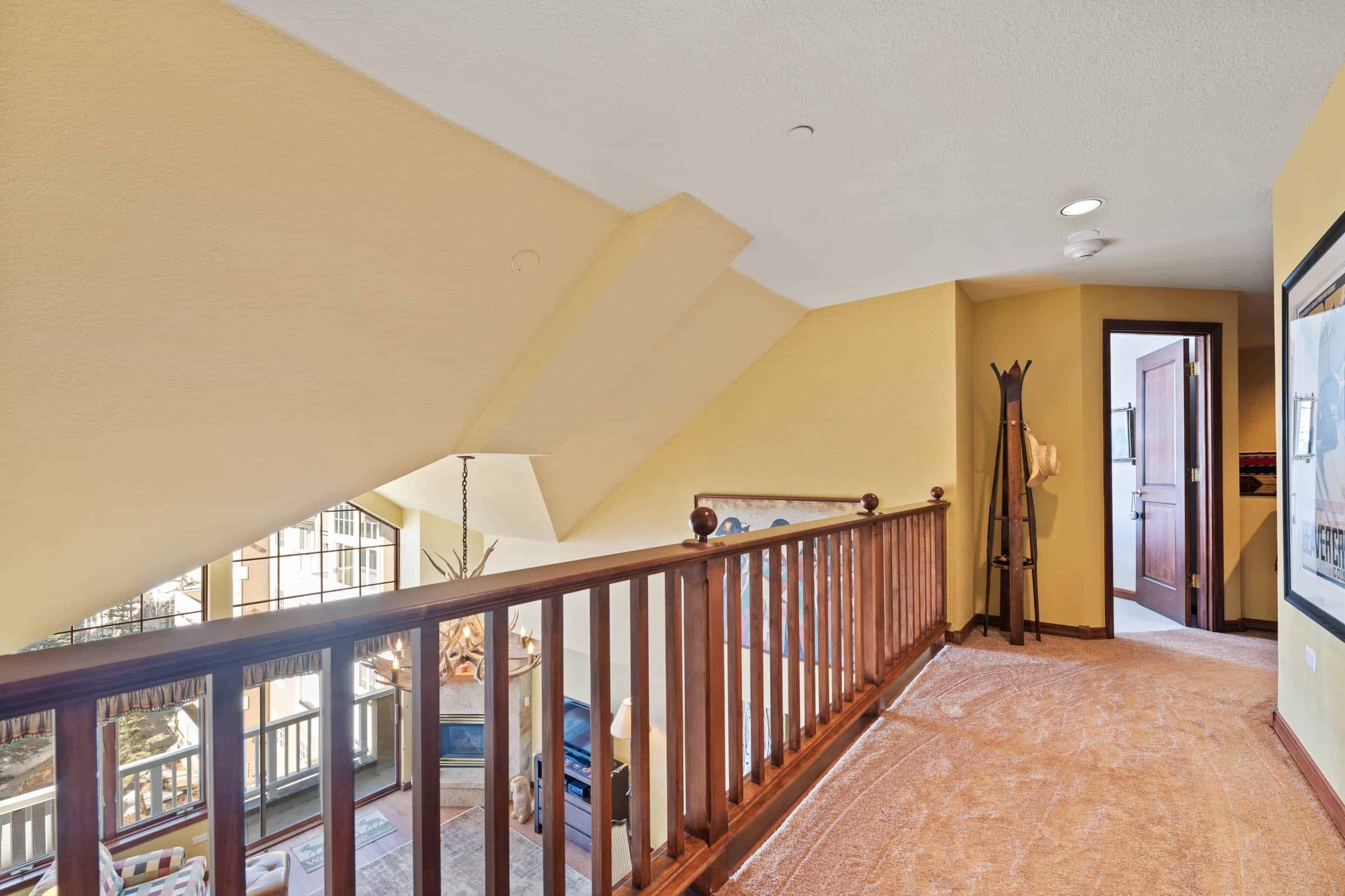 A spacious hallway with a wooden railing, a view of the balcony, and a door leading to another room.