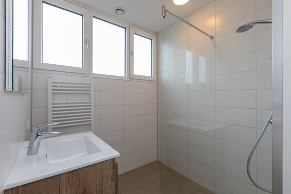 Un baño moderno con un lavabo blanco, ducha y ventana.
