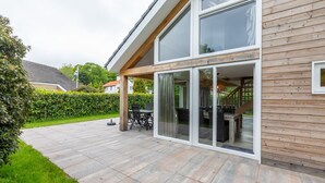 A modern house with a patio, a dining area with outdoor furniture, and a large sliding glass door leading to a covered outdoor space. - Holiday Home near Beach Burgh-Haamstede (Burgh Haamstede)