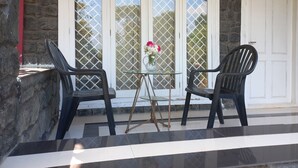 A patio with two black chairs, a small glass table, and a vase with flowers. - Manikkal Outhouse Cottage Wayanad (Mananthavady)