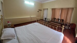 A room with a bed, a ceiling fan, a small table with a vase of flowers, and a seating area with chairs and a sofa. - Manikkal Outhouse Cottage Wayanad (Mananthavady)