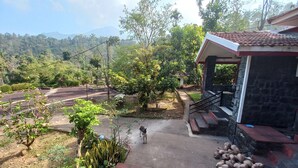 A garden with a pathway leading to a stone building with a red roof. - Manikkal Outhouse Cottage Wayanad (Mananthavady)