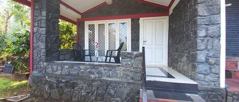 A stone porch with a white door, black chairs, and a small table with a vase.